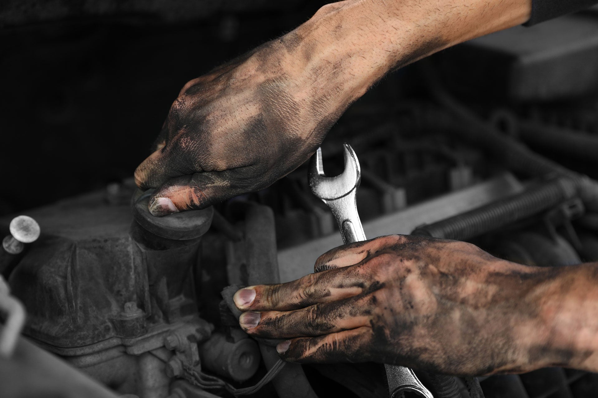 Close-up of hands with dirt on them holding a wrench over an engine.