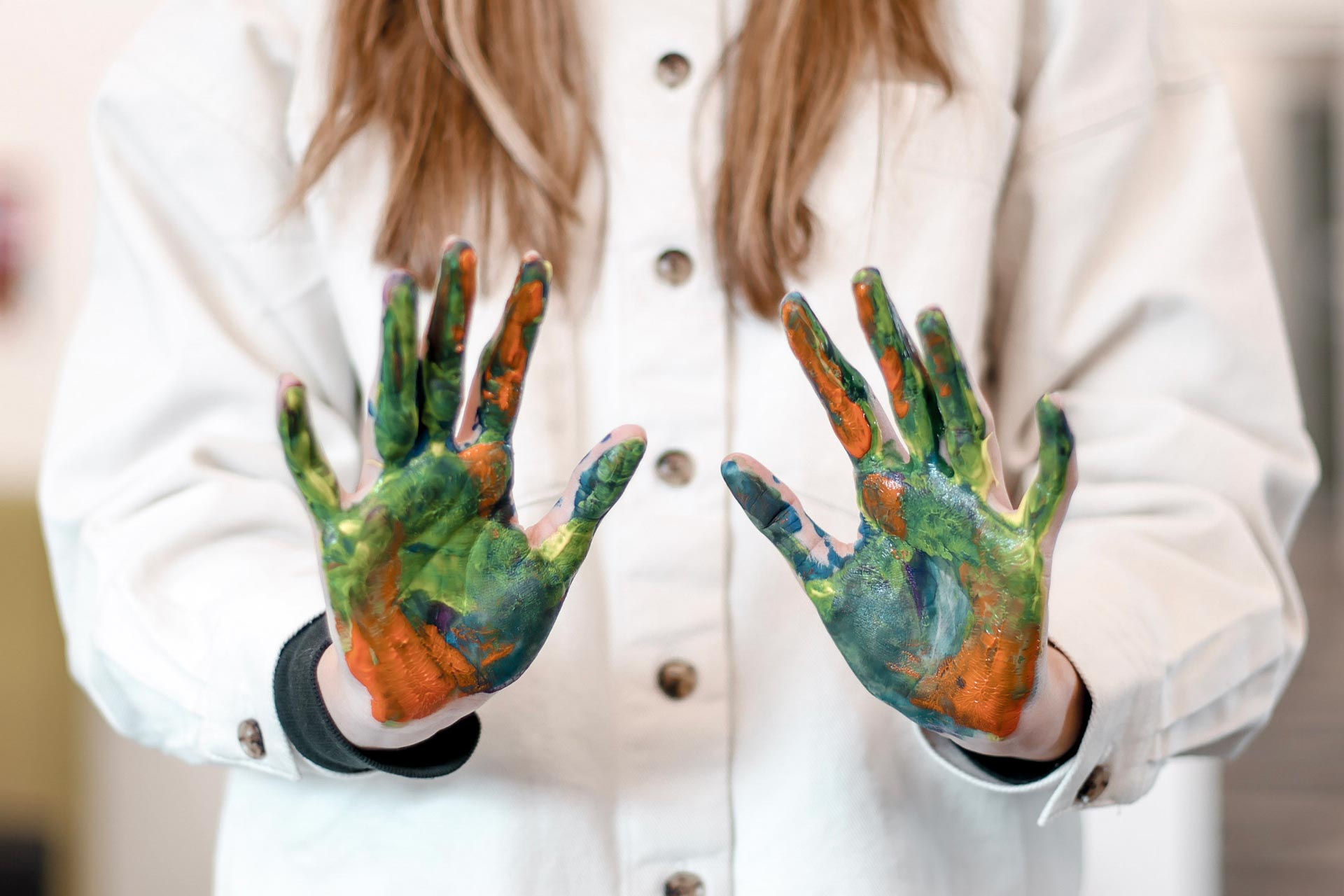 Person wearing a white coat with hands covered in green and orange paint