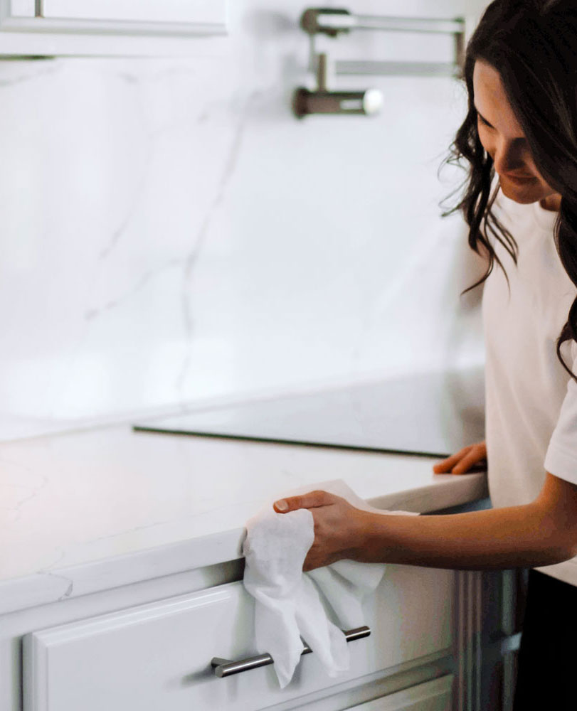 Woman cleaning a kitchen counter with a white cloth.